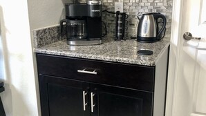A kitchen with dark cabinetry, a granite countertop, a coffee maker, a kettle, and a tiled backsplash. - Disney Dream House, Themed Rooms Pool Arcade BBQ! (Four Corners)
