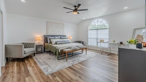 Ein Schlafzimmer mit Bett, Nachttischen, einem Sessel, einem Schreibtisch und einem großen Fenster.