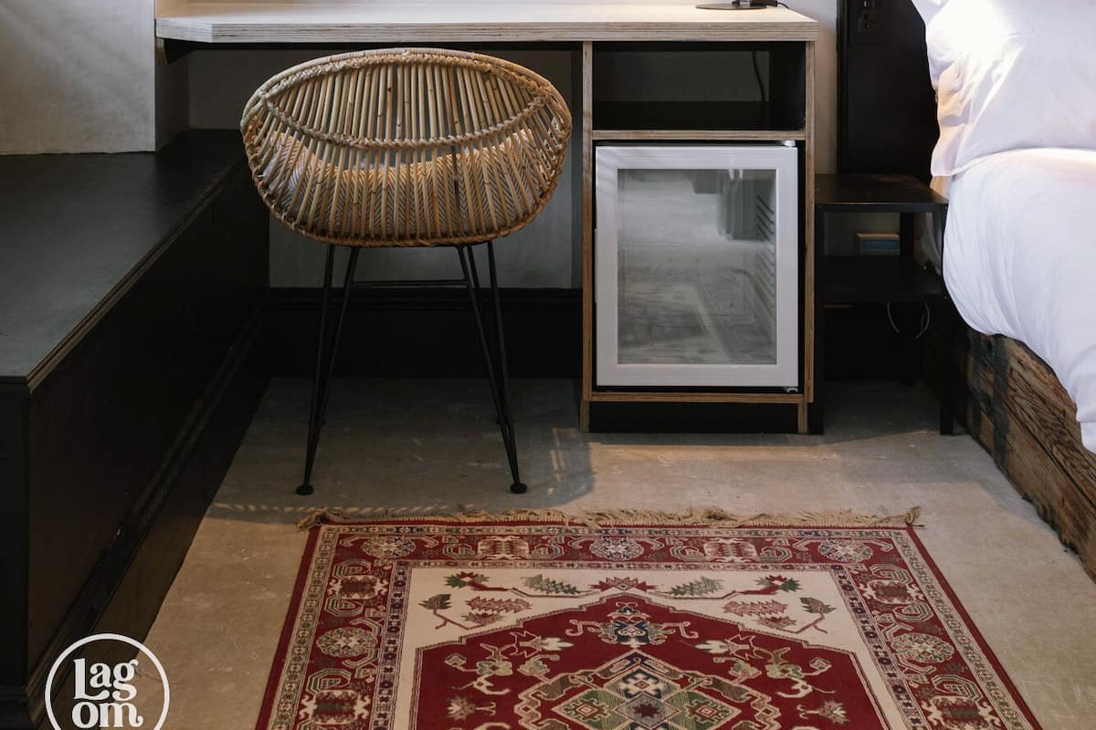 A bedroom with a bed, a bedside table, a chair, a desk, a lamp, and a rug.
