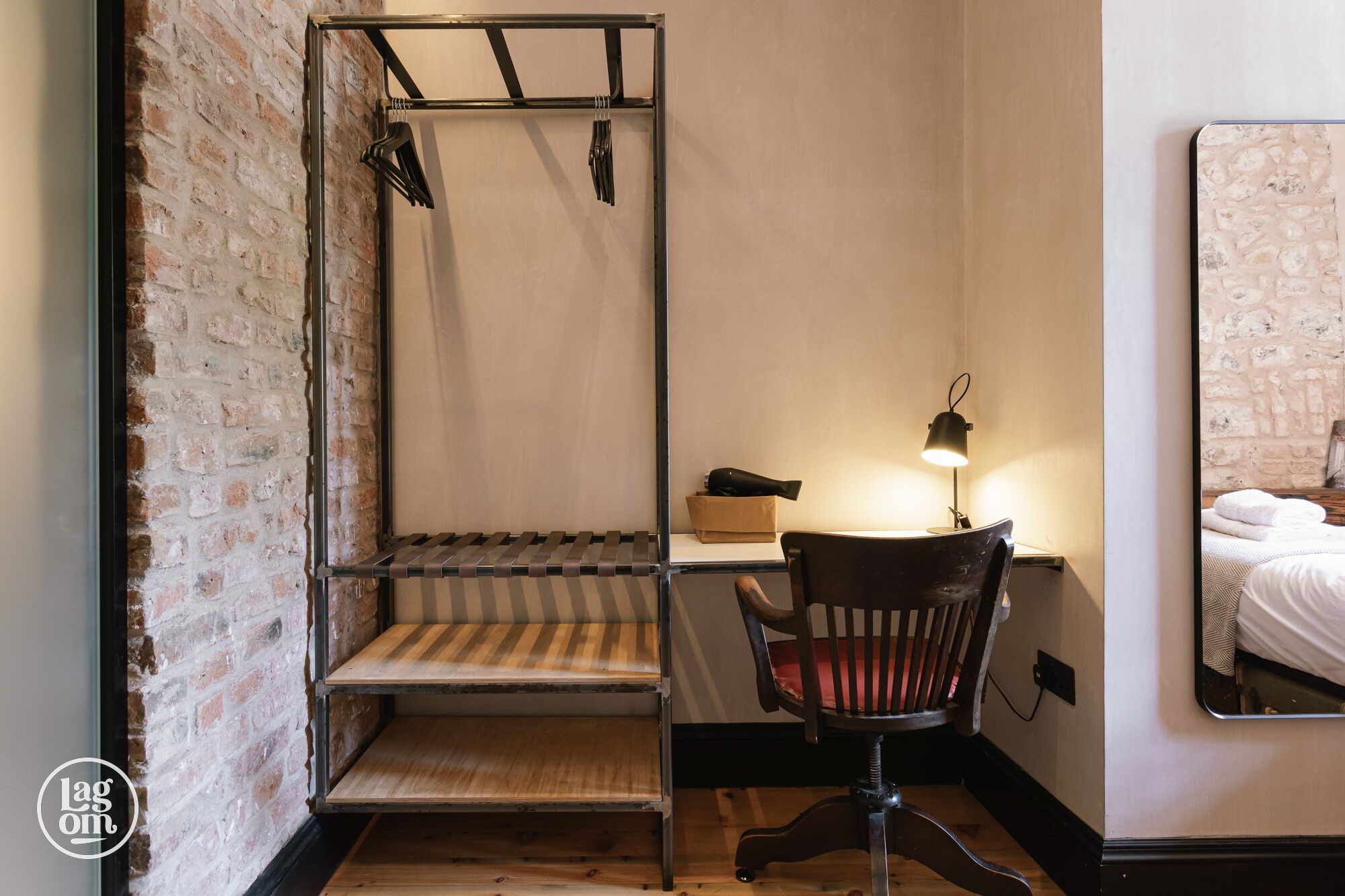 A room with a metal bed frame, a wooden chair, a desk with a lamp, and a mirror on the wall.