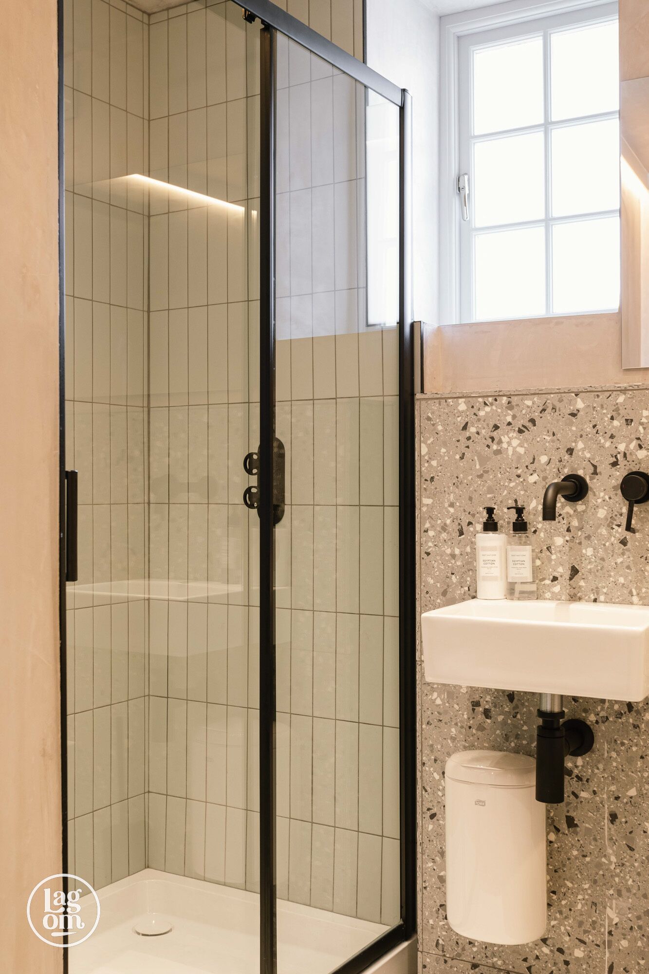 Une salle de bain moderne avec une douche à parois de verre, un lavabo blanc avec un pare-éclaboussures à motifs, et une fenêtre au-dessus du lavabo.