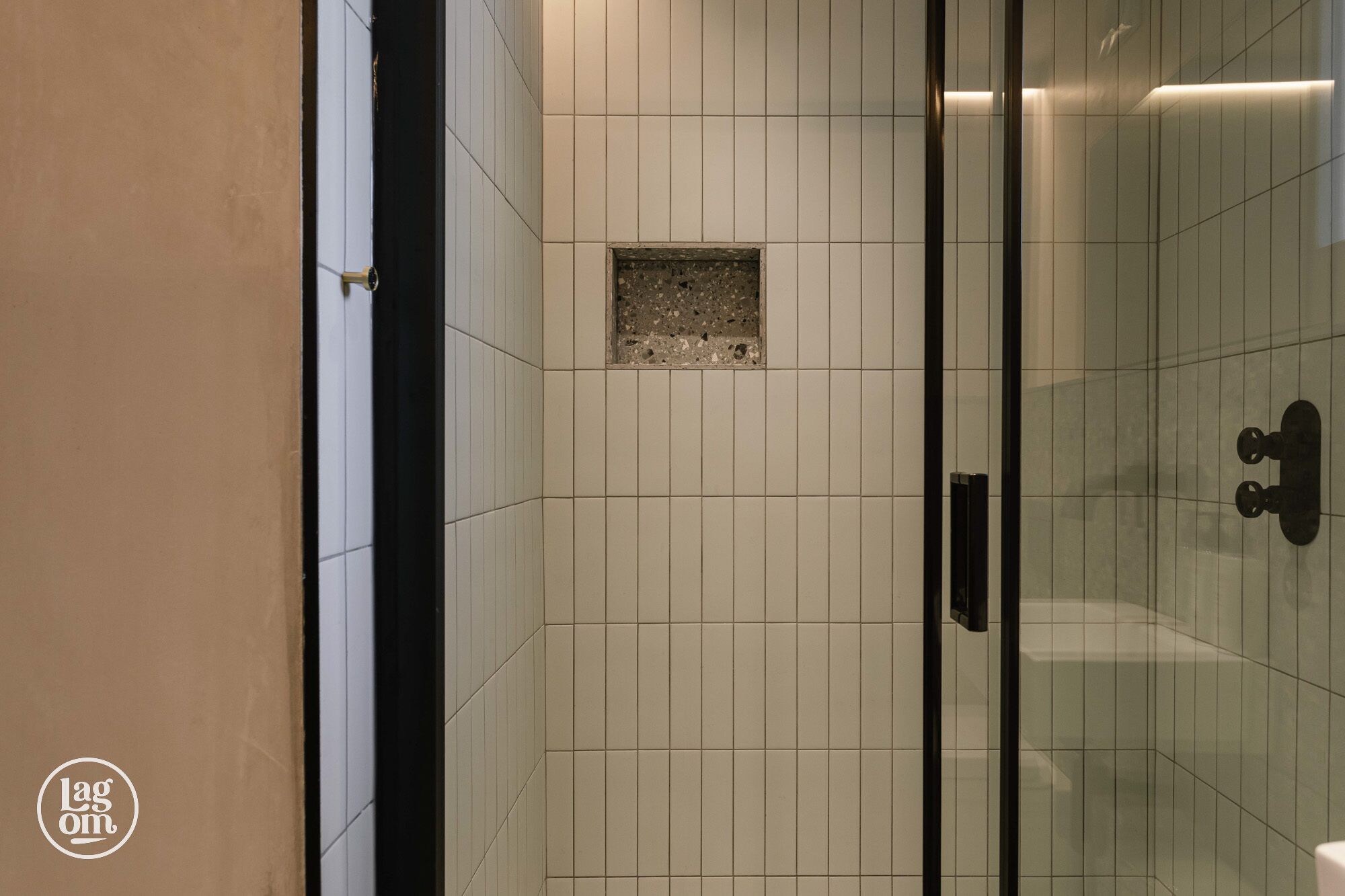 A tiled shower area with a glass door and a small square tile feature on the wall.