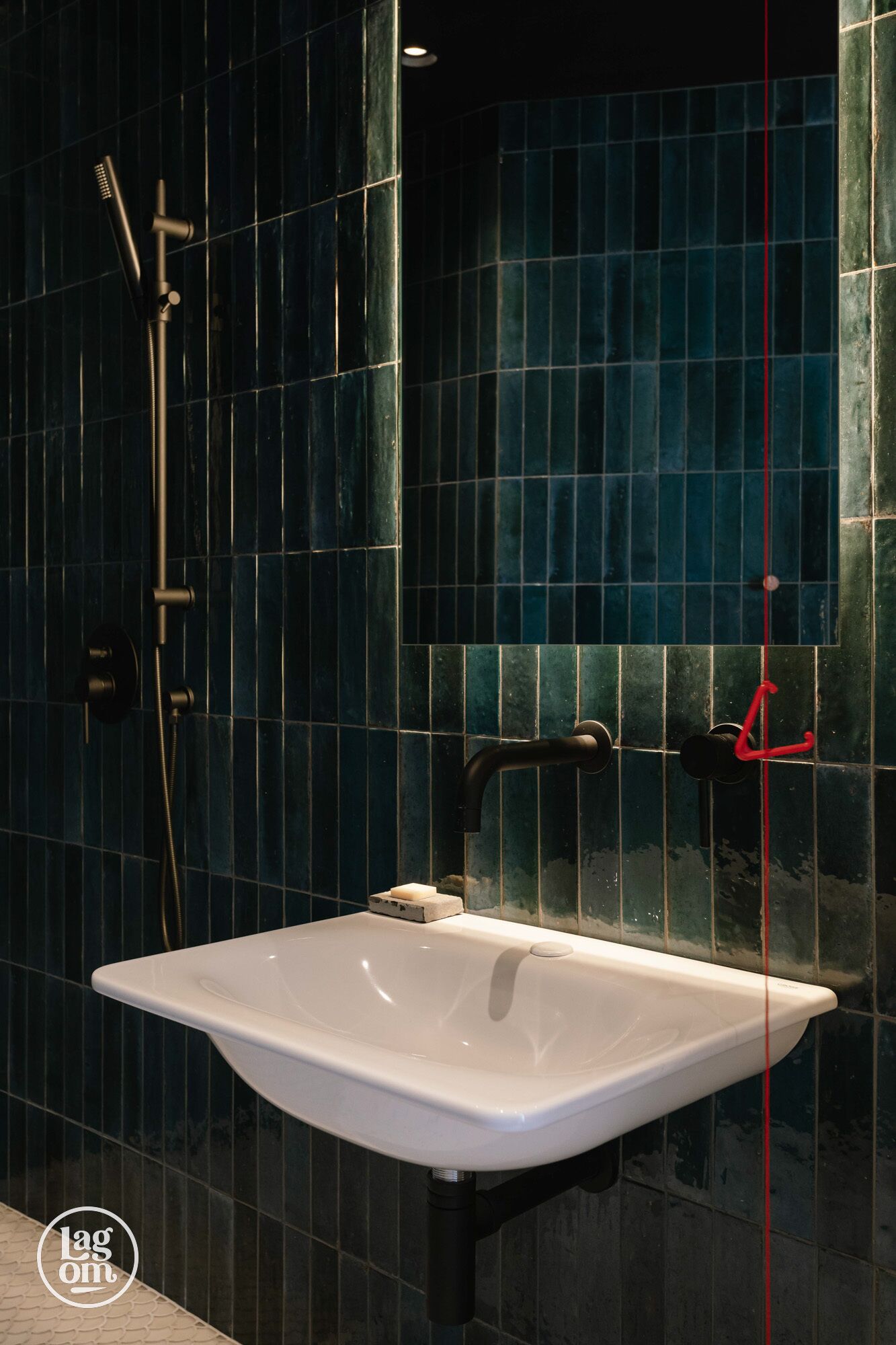 Une salle de bain avec un lavabo blanc, des murs recouverts de carreaux bleu foncé et un espace douche.