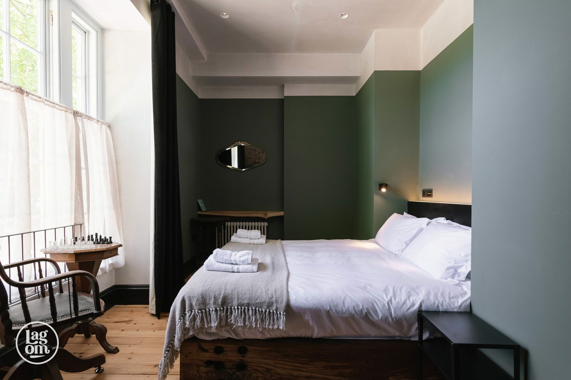 A bedroom with a bed, a chair, a table with chess pieces, and a mirror on the wall.