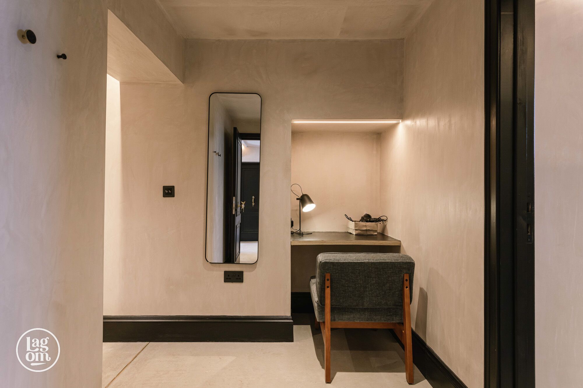 Un couloir avec un miroir, un bureau avec une lampe et une chaise.