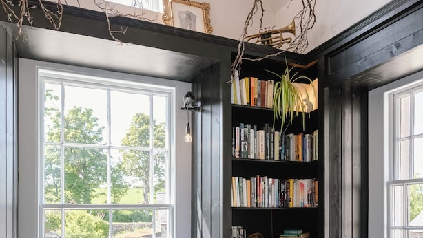 A cozy reading nook with a large window, a bookshelf filled with books, and a decorative plant. - Stay Lagom Lodge (Ballycastle)