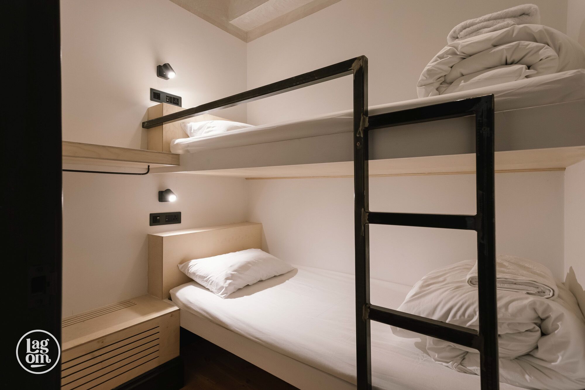 A bunk bed room with a ladder, a bedside table, and a wall-mounted light fixture.