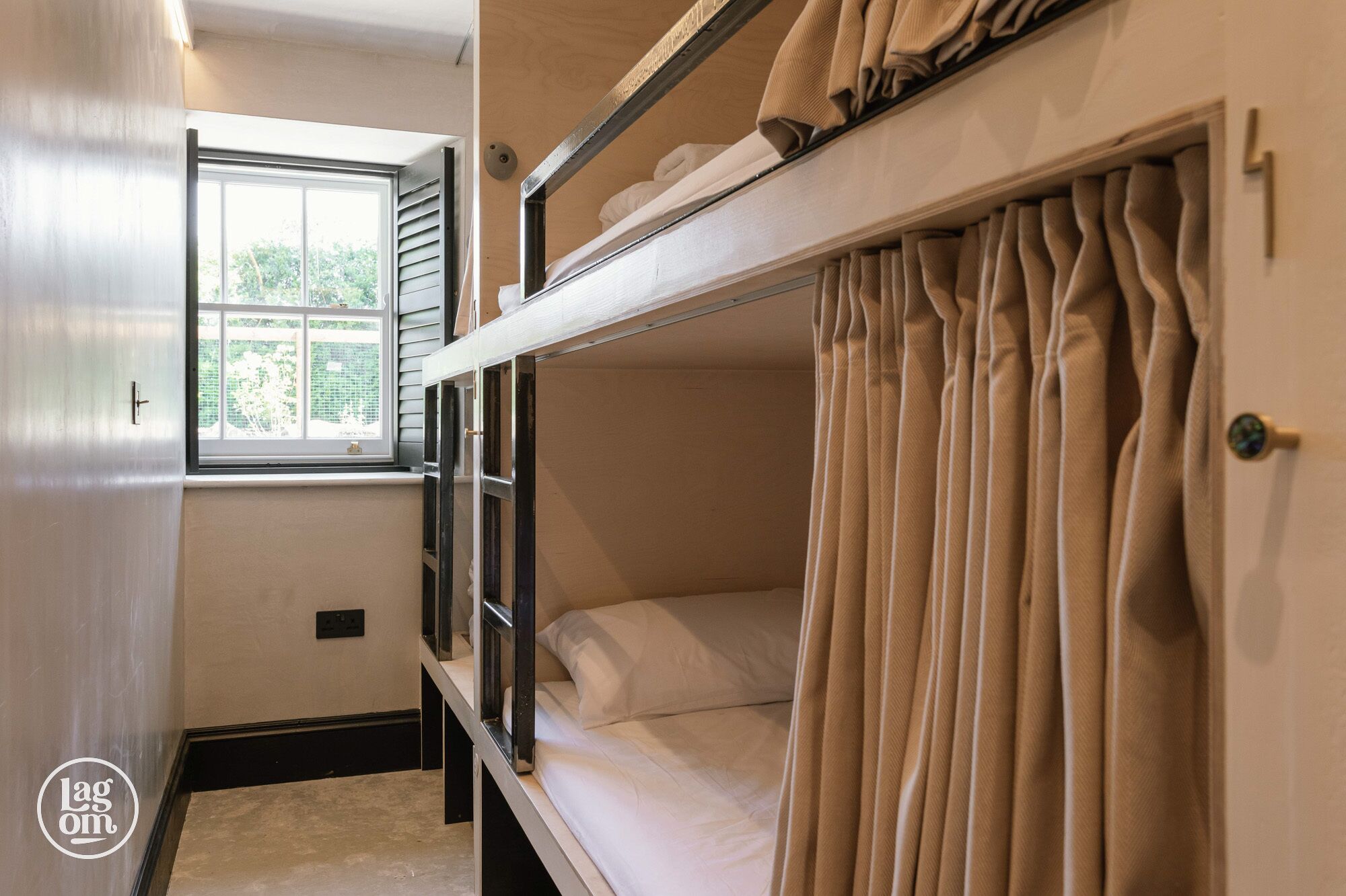 A bunk bed room with a window, curtains, and a door.