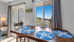 A dining area with a wooden table, starfish placemats, a chair, and a view of the beach through large windows. - Tucked Away at Sea!!! (Gulf Shores)