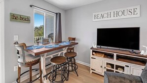A dining area with a wooden table, bar stools, and a TV on a cabinet. - Tucked Away at Sea!!! (Gulf Shores)