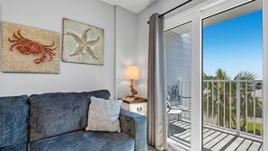 A modern living room with a blue sofa, a small table with a lamp, and two wall art pieces depicting a crab and a starfish. - Tucked Away at Sea!!! (Gulf Shores)