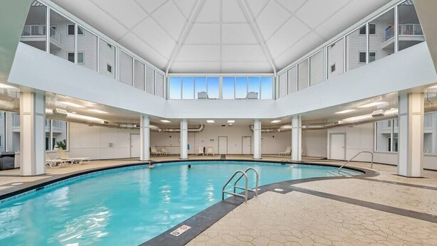 An indoor swimming pool with a clear view of the pool area, a tiled floor, and a high ceiling with windows. - Tucked Away at Sea!!! (Gulf Shores)