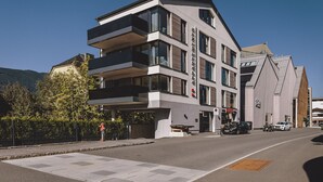 A multi-story building with balconies, a visible entrance, and a parking area with cars. - FP Appartements - Maisi 4, mountain view & summercard (Kaprun)