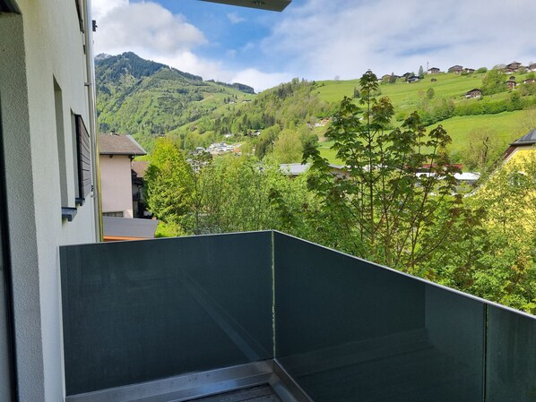Un balcon donnant sur une vallée verdoyante et des maisons éloignées, un ciel dégagé et une montagne en arrière-plan.