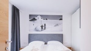 A hotel room with a bed, a large painting of a snowy mountain, and a wooden door. - FP Appartements - Maisi 4, mountain view & summercard (Kaprun)
