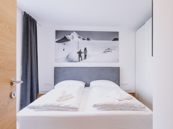 A hotel room with a bed, a large painting of a snowy mountain, and a wooden door.