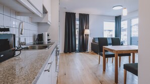 A modern kitchen with white cabinets, a granite countertop, and a dining area with a wooden table and chairs. - FP Appartements - Kitz 5, balcony & summercard (Kaprun)