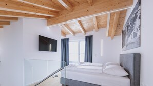 A modern bedroom with a bed, a TV, and a window with curtains. - FP Appartements - Penthouse, Sun terrace & mountain View (Kaprun)