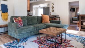 A living room with a green sectional sofa, a brown ottoman, and a colorful rug. - Artful Retreat Near GJs Main St: Dog-Friendly (Grand Junction)