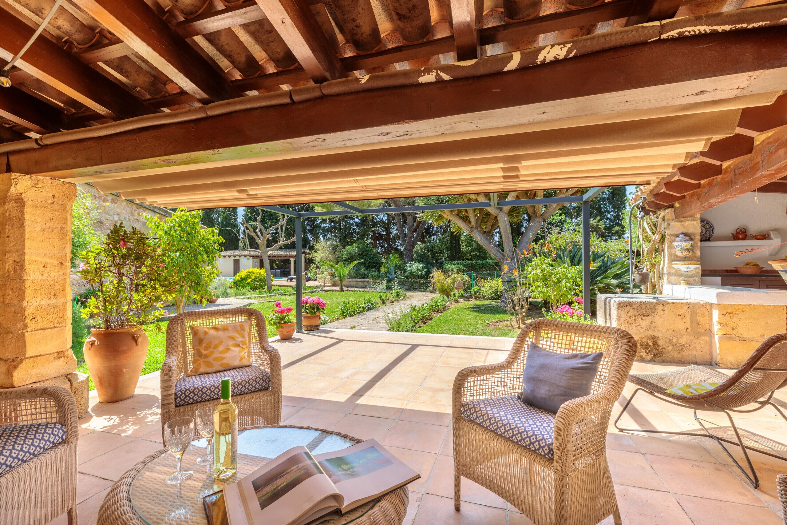 An outdoor patio with wicker furniture, a glass table, and a view of a garden.