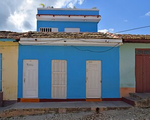 Ein zweigeschossiges Gebäude mit blauer Fassade, weißen Türen und einem Ziegeldach.