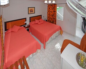 Ein Hotelzimmer mit zwei Betten, einem Schreibtisch, einem Stuhl, einem Ventilator, einem Bild an der Wand und einem Fenster mit Blick.