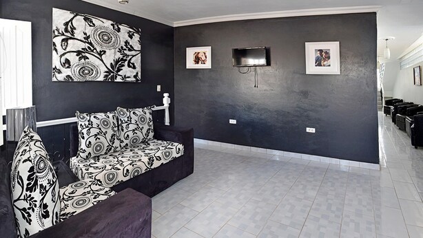 Ein modernes Wohnzimmer mit dunkler Akzentwand, einem schwarz-weißen Sofas und einem an der Wand befestigten Flachbildfernseher, sowie einem Deckenventilator.