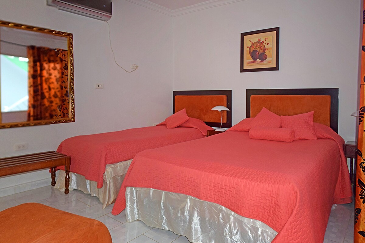 Ein Hotelzimmer mit zwei Betten, einer Bank und einem Spiegel.