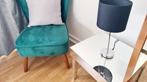 Een smaragdgroene fauteuil met een wit kussen, een klein wit tafeltje met een donkerblauwe lamp, en houten vloeren.