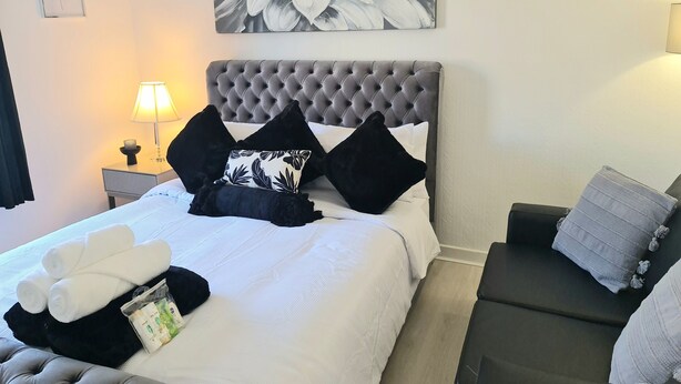 Een net opgemaakt bed met witte lakens, zwart-wit kussens en een grijs hoofdeinde.