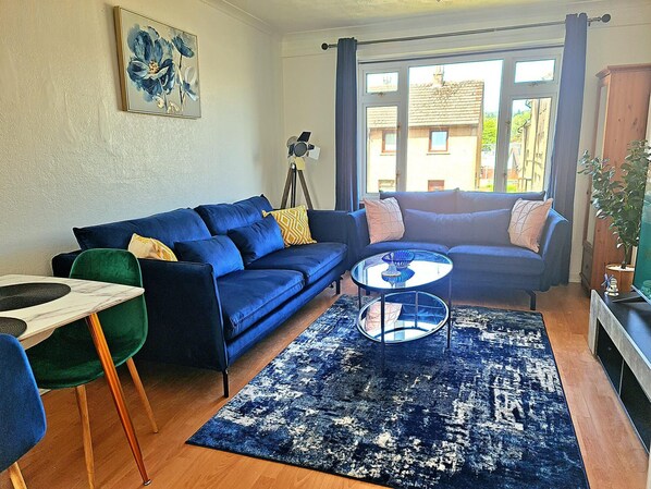 A living room with a blue sofa, a small coffee table, and a floor lamp. - Dundee City Apartment With 3 Bedrooms (Dundee)