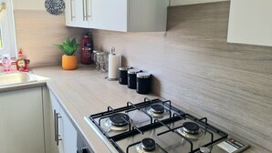 Een keuken met een gasfornuis, witte kastjes, een ananas, een brandblusser en een decoratieve vaas.