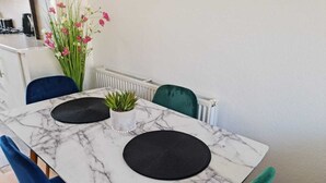 Een eettafel met een marmeren blad, twee zwarte placematen, een kleine potplant en een bloevas.