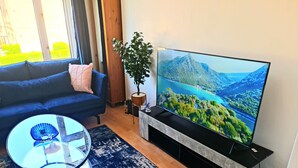 Een woonkamer met een bank, een glazen salontafel, een tv op een meubel en een plant.