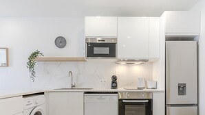 Une cuisine moderne avec des meubles blancs, un four encastré, un lave-vaisselle et un réfrigérateur.