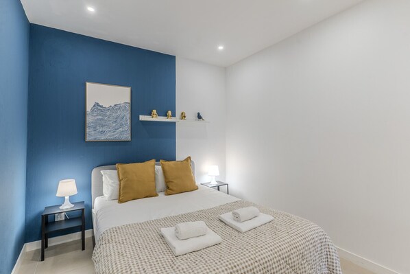 Een slaapkamer met een bed, nachtkastjes, een lamp en een wandplank met decoratieve objecten.