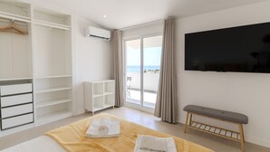 A hotel room with a bed, a bench, a TV, a wardrobe, and a view of the sea.