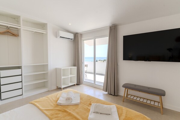 A hotel room with a bed, a bench, a TV, a wardrobe, and a view of the sea.
