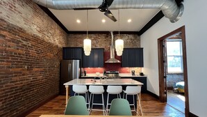 A modern kitchen with a brick wall, stainless steel appliances, and a central island with bar stools. - 1882 Lofts - 301-Downtown 2nd & Church (Nashville)