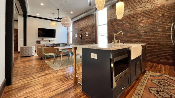 A modern kitchen with a central island, wooden flooring, and exposed brick walls. - 1882 Lofts - 301-Downtown 2nd & Church (Nashville)