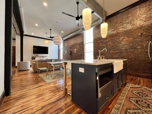 A modern kitchen with a central island, wooden flooring, and exposed brick walls.