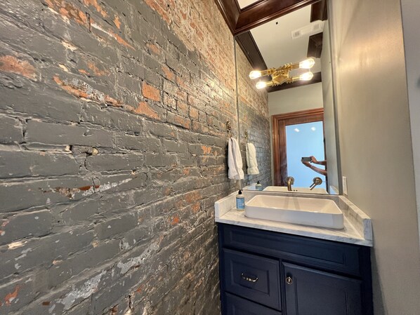A bathroom with a brick wall, a white sink, and a dark cabinet.