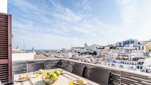 Une terrasse sur le toit, avec une table dressée pour le petit-déjeuner, d’où l’on peut admirer un paysage urbain composé d’immeubles blancs et d’un ciel dégagé.