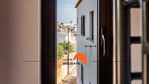 Un étroit passage donnant sur une cour intérieure, d’où l’on aperçoit un bâtiment blanc et un ciel dégagé.