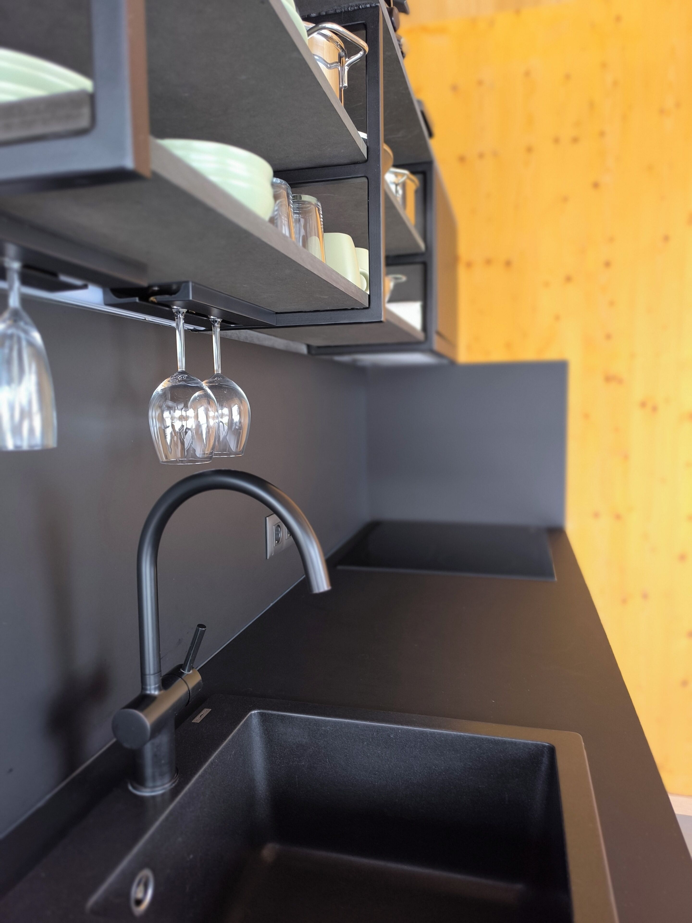 A modern kitchen with a black countertop, a stainless steel sink, and a hanging wine glass rack.