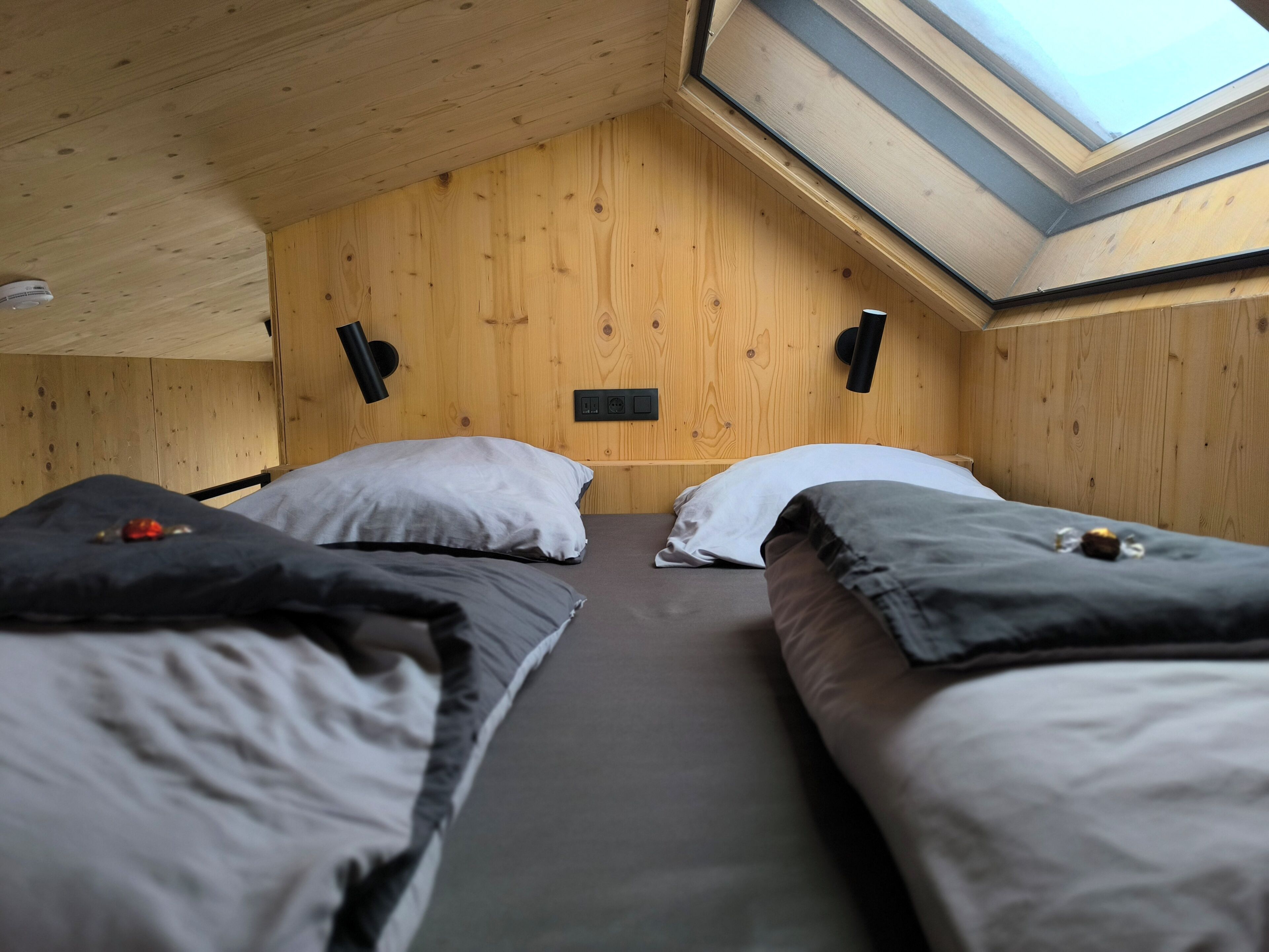 Une pièce avec deux lits, une lucarne, des murs en bois et un petit panneau de distribution téléphonique noir.