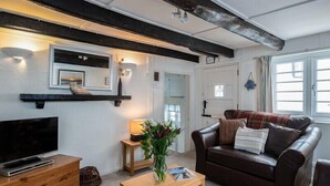 A cozy living room with a dark leather sofa, a wooden coffee table, and a flat-screen TV on a wooden dresser. - St Samson (Port Isaac)