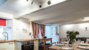 A compact kitchen with a built-in oven, a dining table set for four, and a window with curtains. - St Samson (Port Isaac)