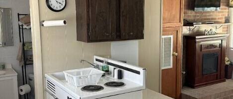 A compact kitchen with a white stove, wooden cabinets, and a small trash bin.