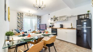 Et moderne køkken med et sort køleskab, hvide skabe og et spisebord i glas.